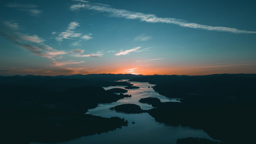 Prowall Free Wallpaper | A breathtaking aerial shot showcasing a calm river winding through hills at sunset, with a vivid sky.