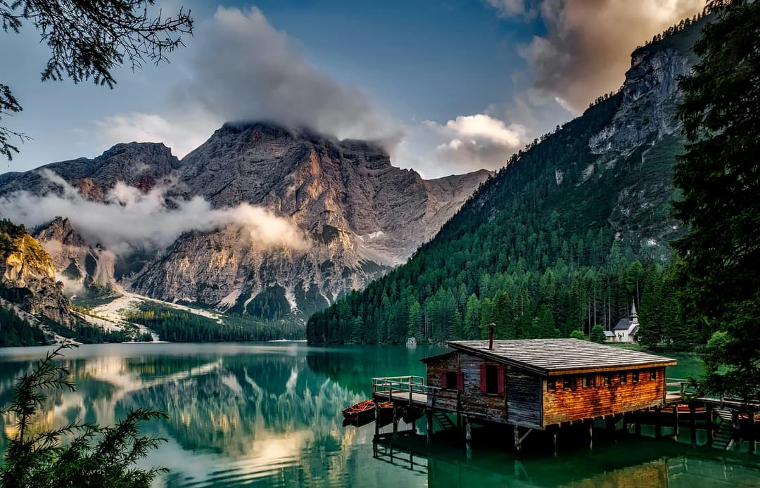Prowall Free Wallpaper | Peaceful mountain lake scene featuring a rustic boathouse and stunning reflections.