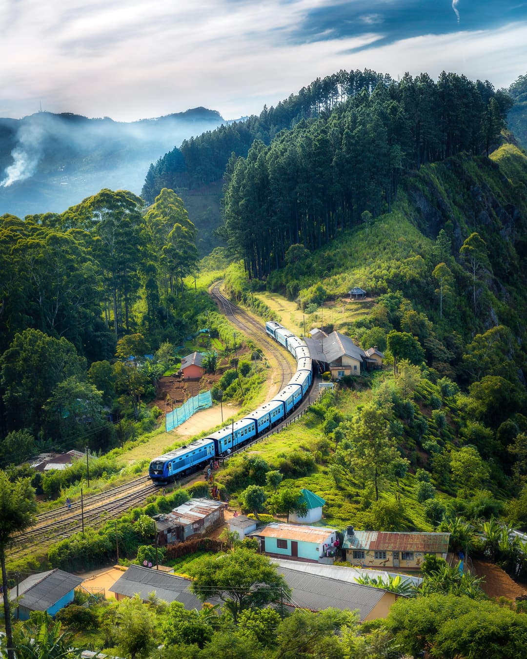 Prowall Free Wallpaper | Aerial view of a picturesque train winding through lush green hills and rural houses.