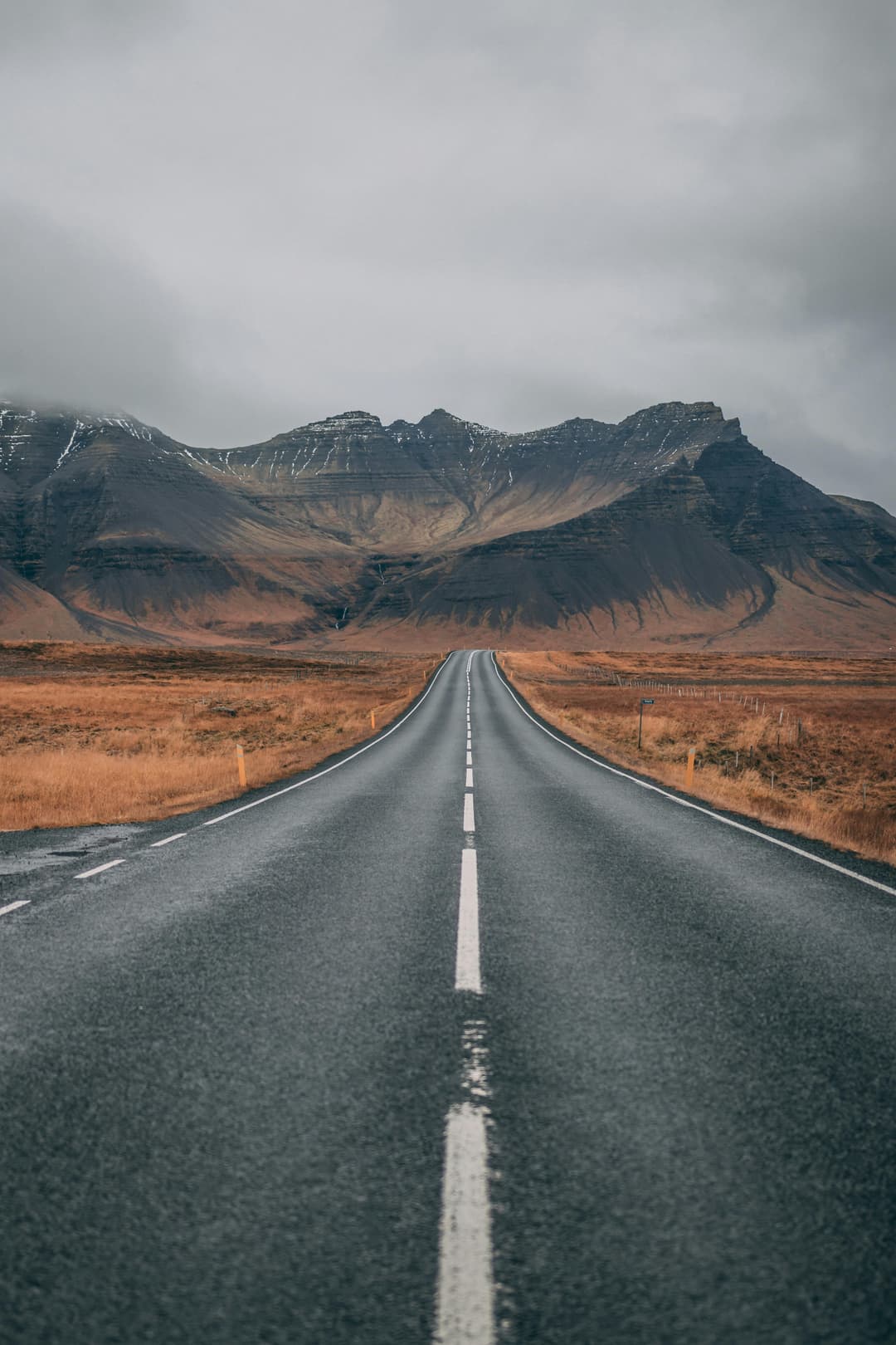 Prowall Free Wallpaper | A scenic empty road stretches into snow-capped mountains under cloudy skies, offering a sense of adventure and tranquility.