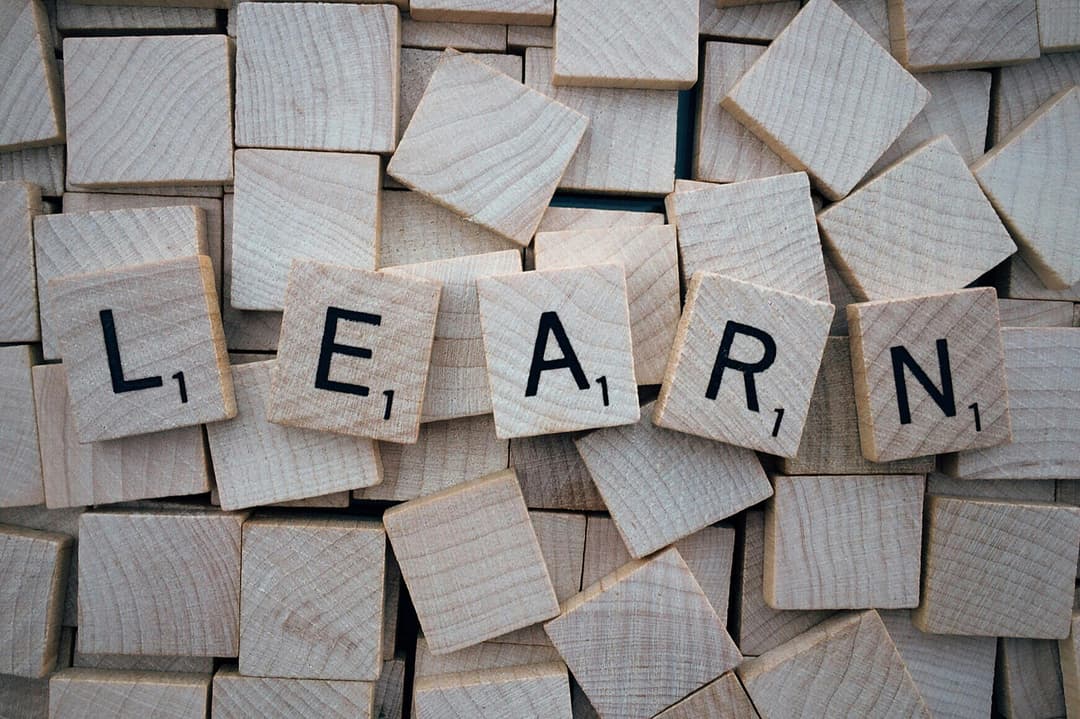 Prowall Free Wallpaper | Wooden letter tiles arranged to spell 'learn' on a background of scattered tiles.