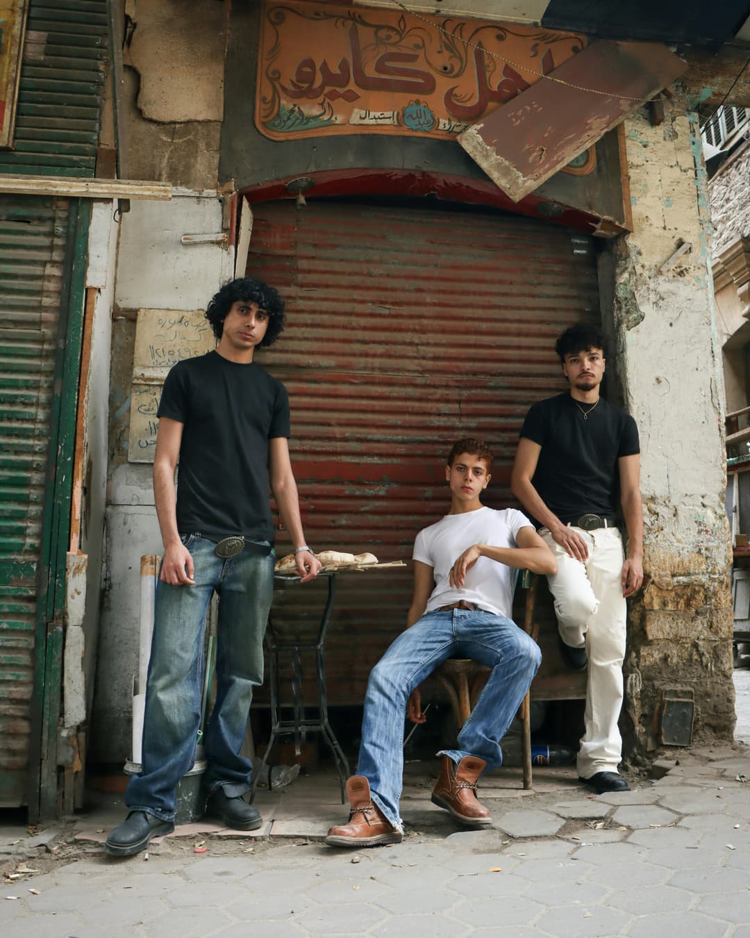 Prowall Free Wallpaper | Three young men pose in front of a closed shop in Cairo, showcasing casual fashion.