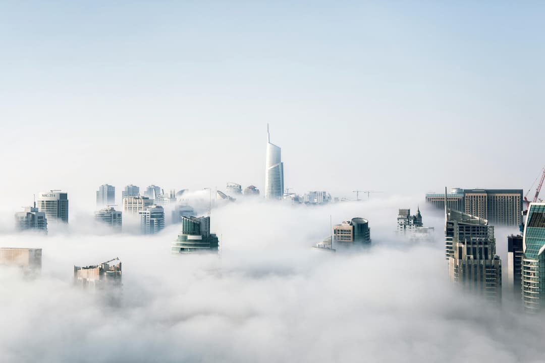 Prowall Free Wallpaper | A stunning view of Dubai skyscrapers emerging through a blanket of fog, showcasing modern architecture.