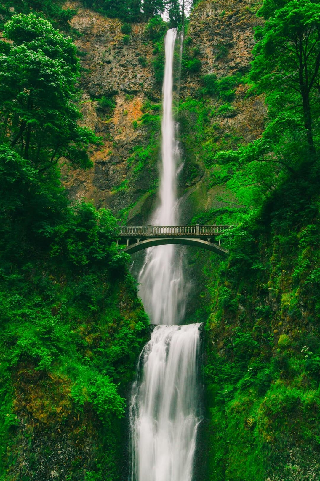 Prowall Free Wallpaper | Captivating waterfall cascading through lush greenery and a scenic bridge.