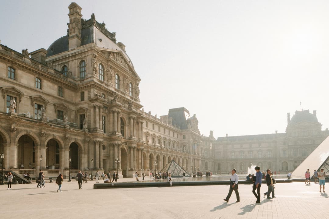 Prowall Free Wallpaper | People walking at Louvre Museum courtyard with iconic pyramids in Paris during daytime.