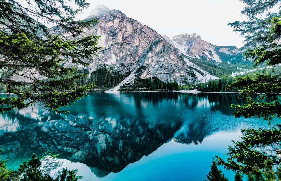 Prowall Free Wallpaper | Serene mountain lake with stunning reflections in Braies, Italy, surrounded by trees.