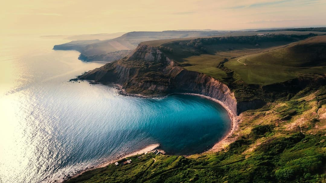 Prowall Free Wallpaper | A breathtaking aerial view of coastal cliffs with turquoise water and lush landscapes.