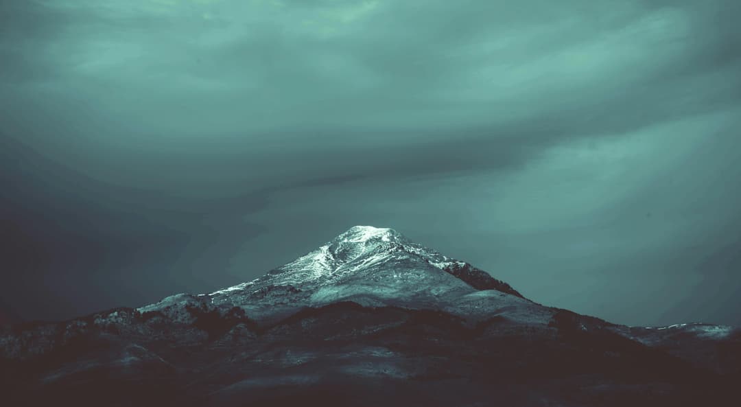 Prowall Free Wallpaper | A dramatic snow-capped mountain peak in Algeria set against a moody sky, perfect for winter landscapes.