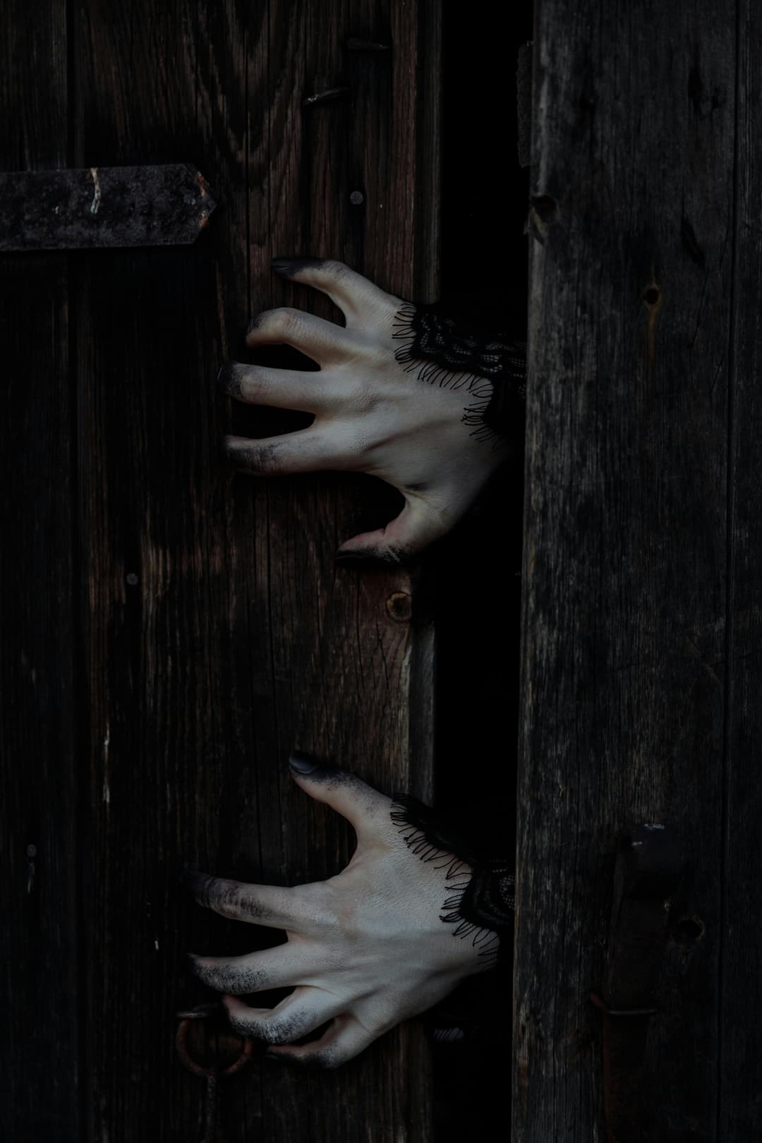 Prowall Free Wallpaper | Eerie white hands with black nails reach through a dark wooden door, perfect for Halloween themes.