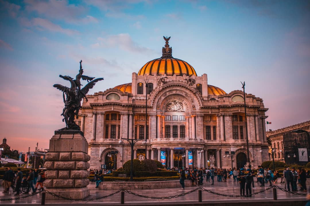 Prowall Free Wallpaper | Vibrant sunset at the historic Palacio de Bellas Artes in Mexico City, bustling with tourists.