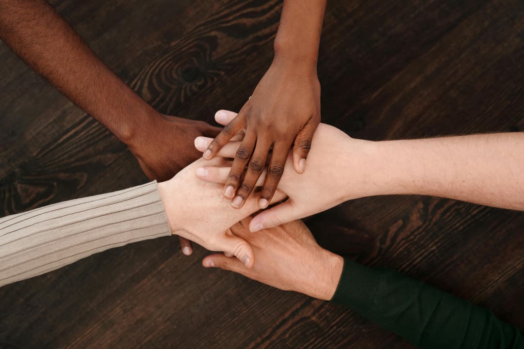 Prowall Free Wallpaper | A diverse group of hands joining together, symbolizing unity and teamwork on a wooden surface.