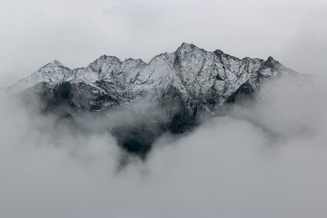 Prowall Free Wallpaper | A breathtaking view of snow-covered mountain peaks surrounded by dense fog, creating a mystical landscape.