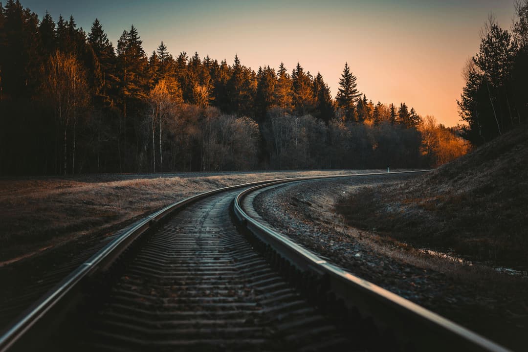 Prowall Free Wallpaper | A serene view of a railway track in a forest at sunset with Autumn colors.