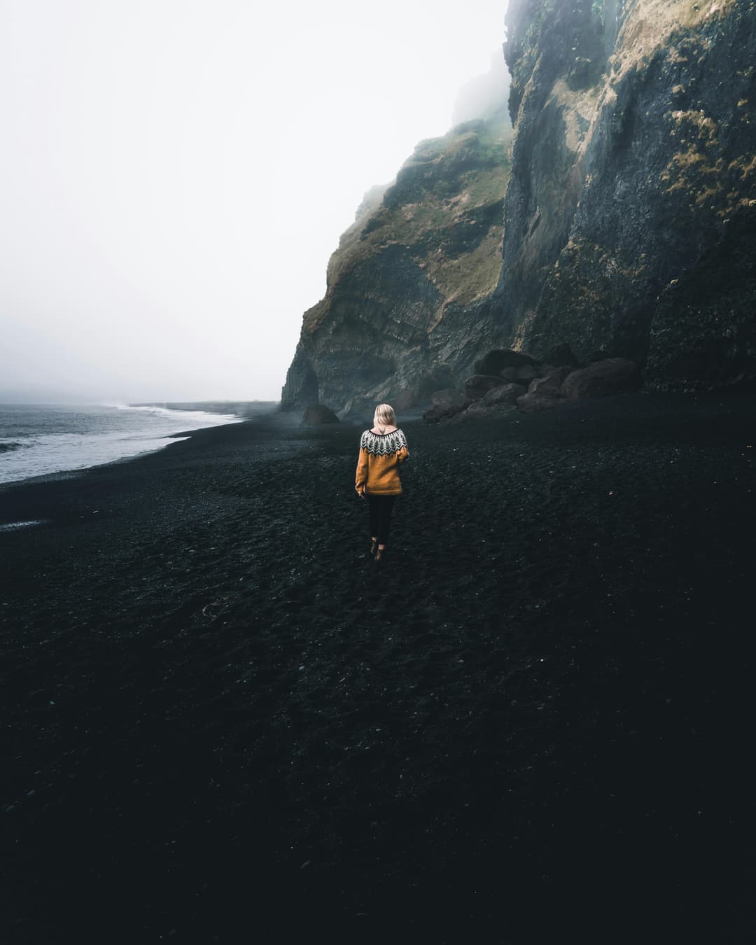 Prowall Free Wallpaper | Woman walking alone on the misty black sand beach in Iceland's dramatic coastal landscape.